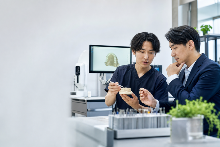 歯科技工所で歯科技工士と採用担当者がCADと補綴物を確認する様子